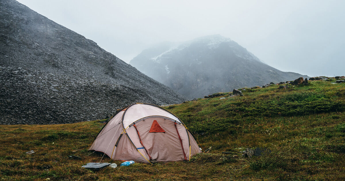 A small, light pink tent on a lush green hill. There are multiple mountains in the background.